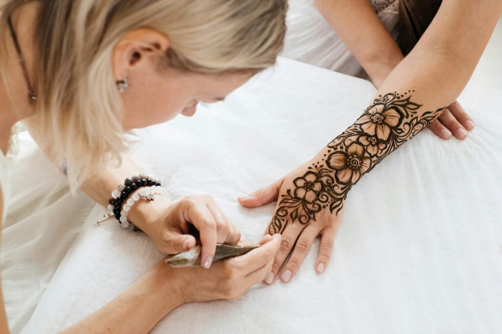 female hands with mehendi pattern of flowers, artist painting with henna